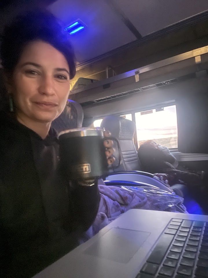 Anya Metcalfe with a coffee mug and a laptop, working while traveling at dawn.